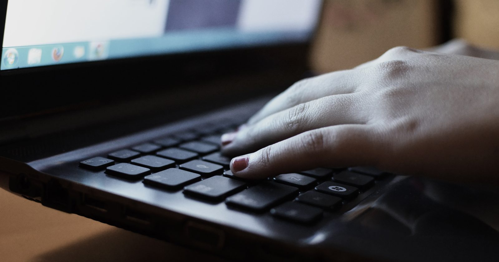 Dłonie osoby piszącej na klawiaturze laptopa leżącego na biurku.